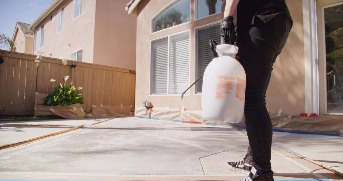 Person spraying concrete in a residential backyard, preparing for color application as part of concrete restoration.