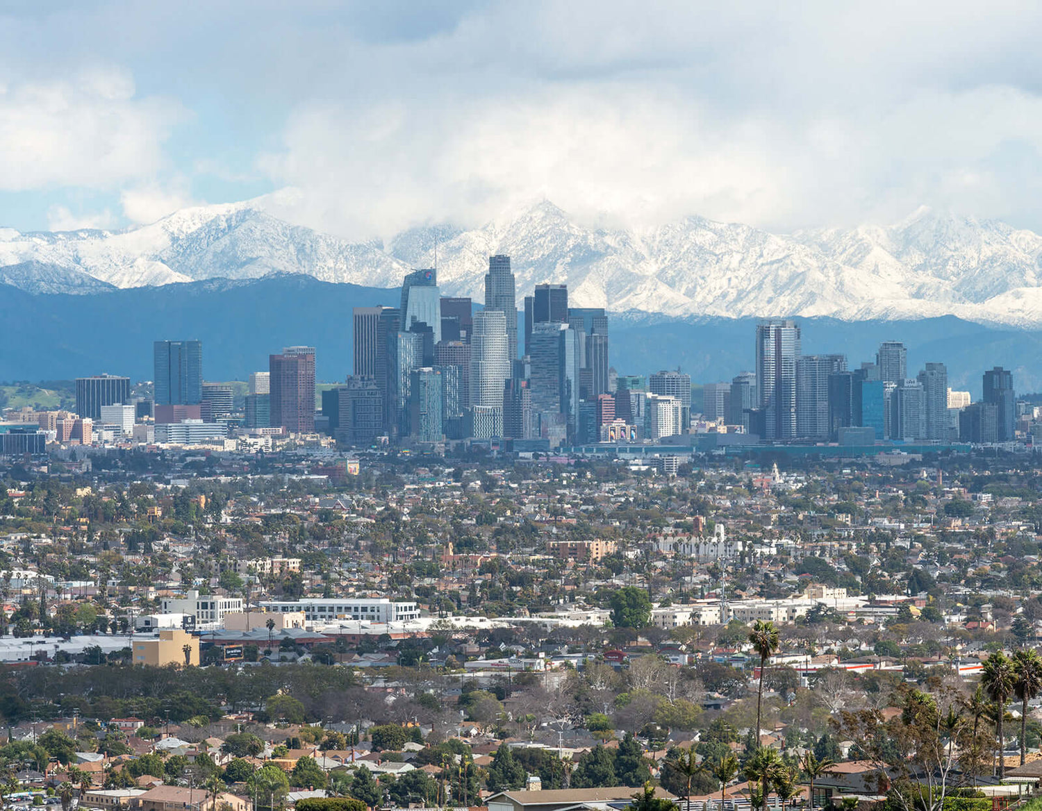Los Angeles skyline with snow-capped mountains in the background on a cloudy day.