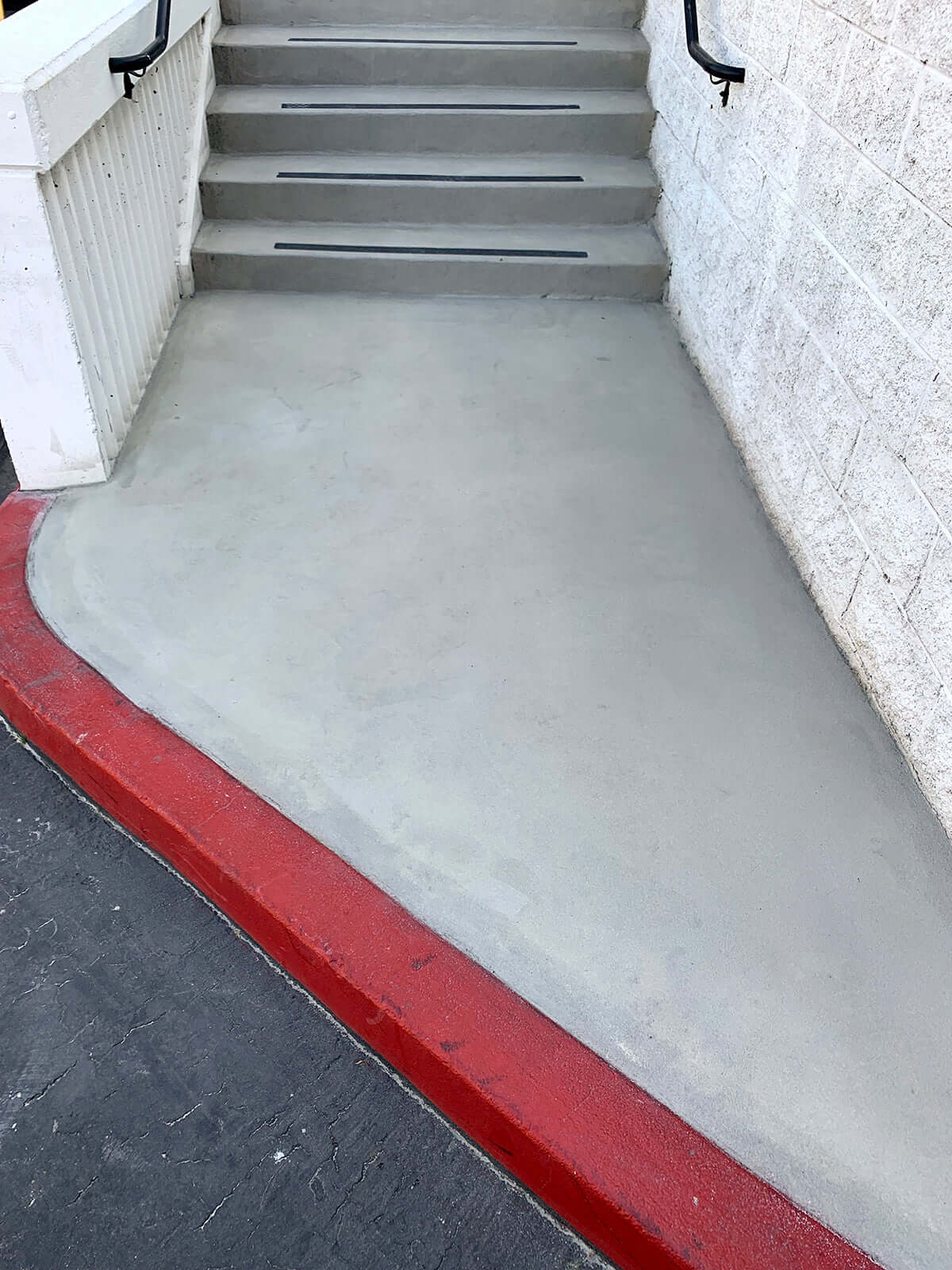 Freshly restored concrete walkway and steps with red curb detailing, demonstrating expert concrete restoration work.