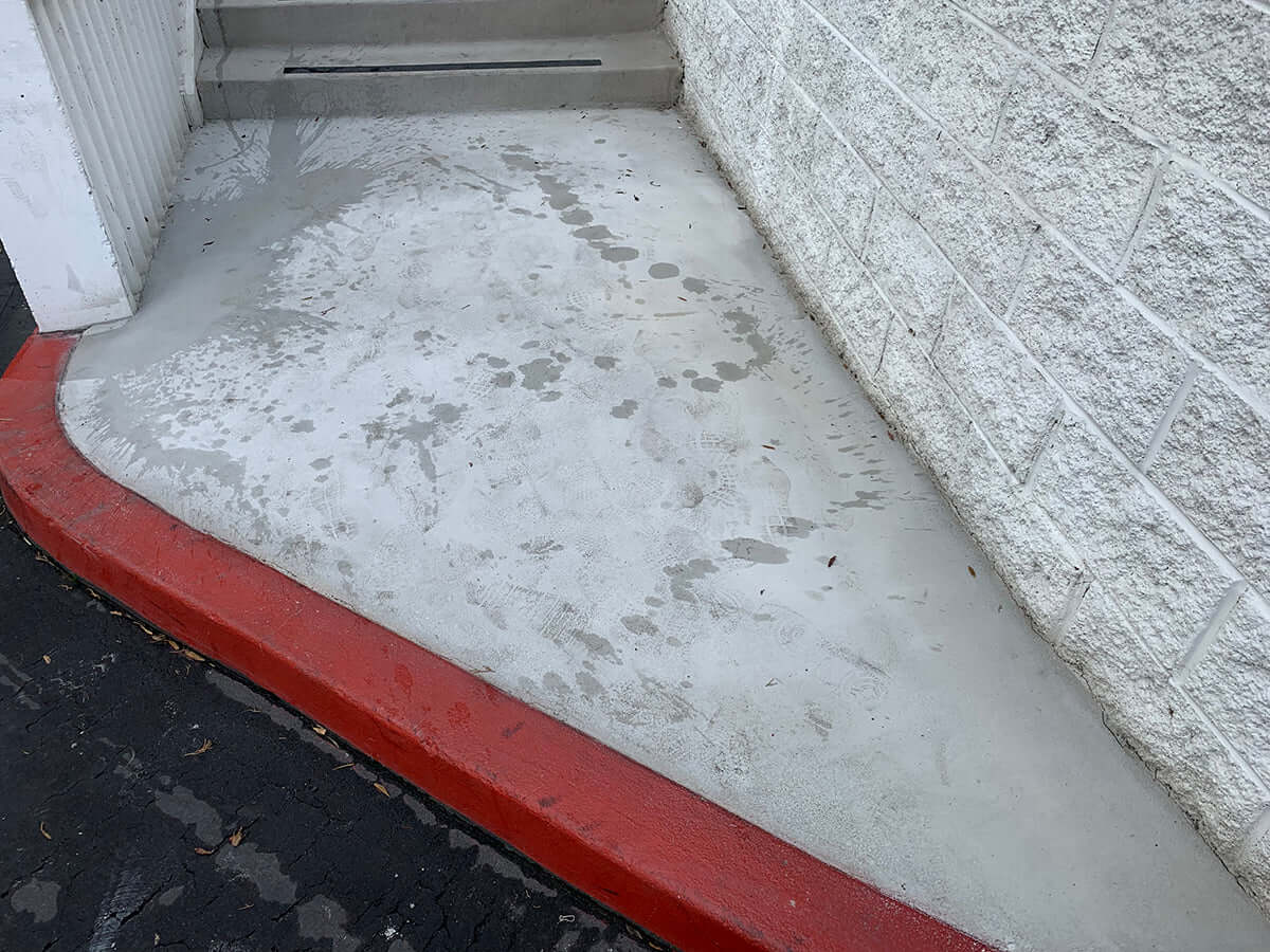 Newly restored concrete pathway next to a building wall and red curb.