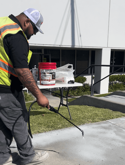 Worker applying Like-Nu Concrete mix for restoration on a sidewalk with spray equipment.