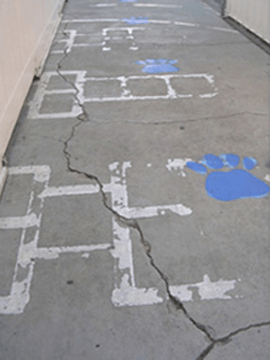 Cracked concrete sidewalk with hopscotch game and blue paw prints, ideal candidate for concrete resurfacing.